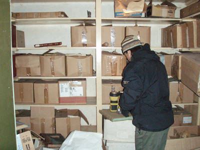 Photo of person with striped hat standing in front of boxes on shelves.